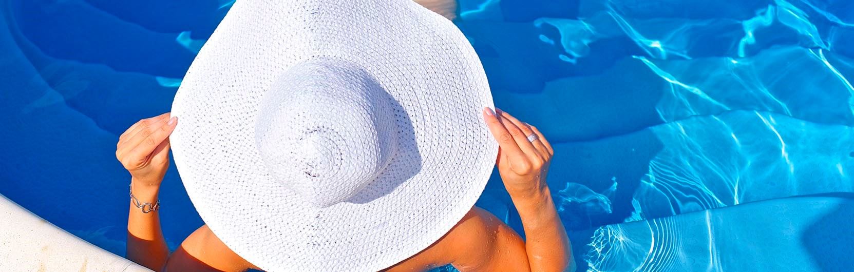 Mujer en una piscina con un gran sombrero blanco que la tapa