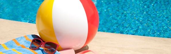 Balón para piscina, gafas para sol y tohalla al lado de una piscina
